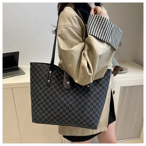 Detail of black tote bag with gray M-pattern and leather straps on shoulder