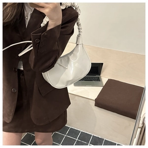 Detailed view of white patent leather cloud bag with ruched handle on woman shoulder