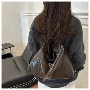Detail view of large dark brown retro leather backpack with metal buckles on a model