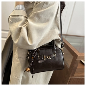 Detail view of deep brown leather Boston bag featuring gold horsebit and bell charm