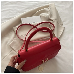 Détail du sac rouge à bandoulière avec logo D doré sur un blazer blanc et livres