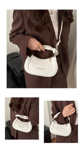 Close-up of white crescent crossbody bag with knotted handle and gold zipper detail