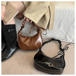 Detail of elegant pleated crescent bags in brown and black leather with ribbon accents