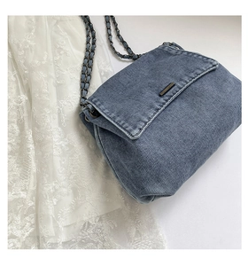 Detail of denim crossbody bag with chain strap and metal bar closure on white lace