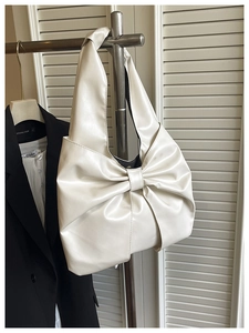 Détail d'un sac à main beige présentant un grand nœud et une texture en cuir PU mat