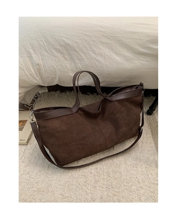 Detail of dark brown suede tote bag with leather straps on a soft textured carpet