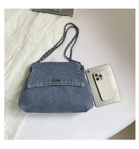 Blue denim shoulder bag with chain strap and phone for size reference shown on white surface