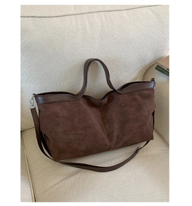Detailed texture of dark brown matte suede tote bag with smooth leather trim on a sofa