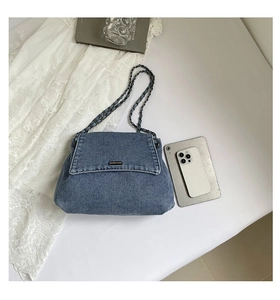 Detail view of blue washed denim tote bag with black metal chain and leather strap