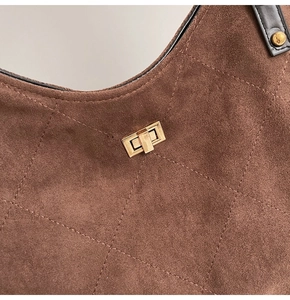 Détail du sac à main en daim marron avec surpiqûres matelassées et fermoir doré
