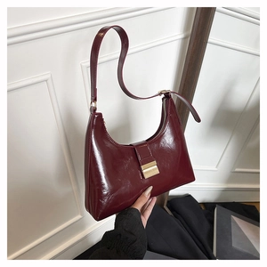Detail of high-gloss burgundy underarm bag with gold buckle and secure zip closure
