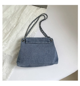 Detail of blue denim flap bag with metal chain strap and washed fabric texture
