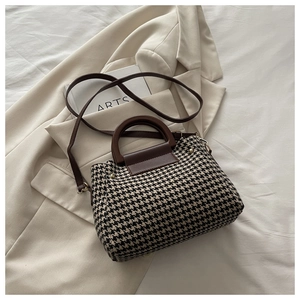 Detailed view of houndstooth handbag featuring a round wooden handle and slim shoulder strap