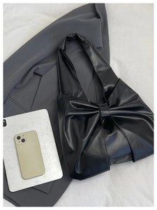 Sac à main noir brillant avec grand nœud placé sur un blazer de bureau gris élégant