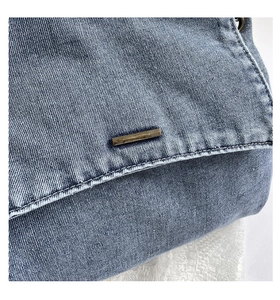 Close-up of blue denim tote bag featuring bronze metal buckle and precise stitching details
