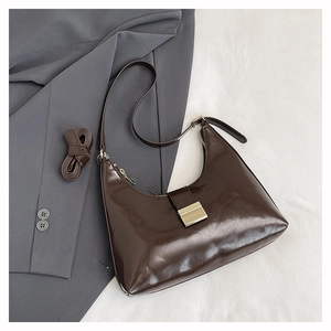 Detail of dark brown patent leather dumpling bag with metal buckle and extra strap