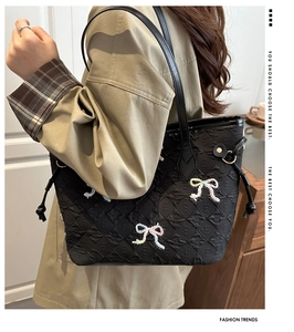 Detail of black quilted tote bag featuring pearl bow embroidery and logo texture