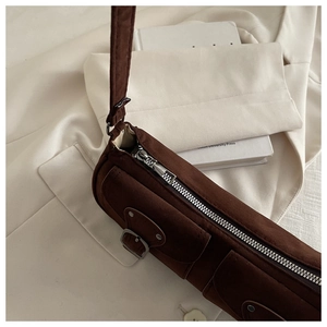 Detail view of brown suede shoulder bag with metal zipper and buckle on white blazer
