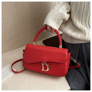 Détail du sac en cuir rouge montrant le logo D doré et la texture lisse du sac à main