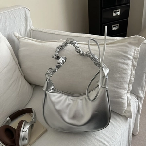 Sac demi-lune argenté avec poignée froncée et nœud décoratif sur canapé blanc