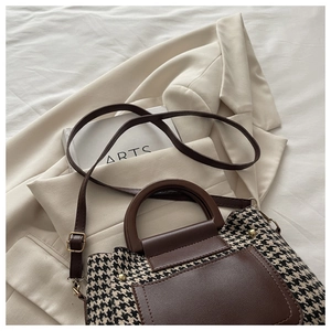 Close-up of houndstock fabric detail and brown leather handle on a vintage handbag