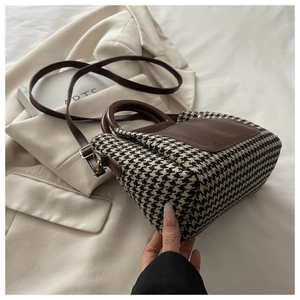 Detail of houndstooth crossbody bag with brown leather handles and gold-tone hardware