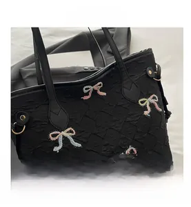 Macro detail of black ruched tote bag featuring colorful bow embroidery and gold hardware