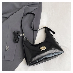 Detail of black patent leather underarm bag with gold buckle on grey blazer background