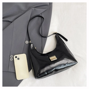 Close-up of a black glossy hobo bag with a gold metal clasp on a grey blazer