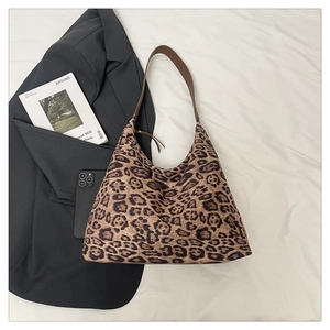 Détail d'un sac hobo léopard avec bandoulières en cuir sur un fond de tissu blanc