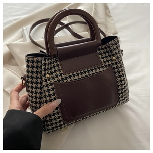 Close-up of vintage houndstooth handbag with brown leather trim and metal rivets
