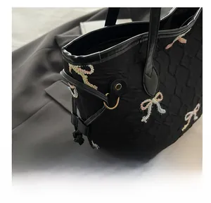Close-up of black quilted tote bag featuring colorful 3D bow embroidery and drawstring detail