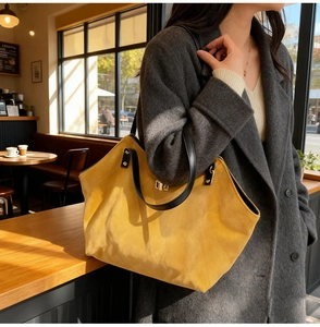Detail of yellow faux suede tote bag with black leather handles and gold metal lock