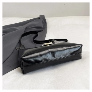 Detail of black patent leather shoulder bag with metallic clasp and adjustable strap