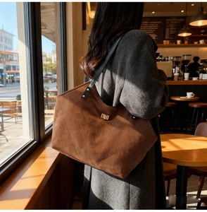 Close-up of quilted brown suede tote bag featuring a golden clasp and black leather straps