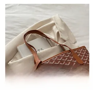 Close-up of brown plaid pattern tote bag with leather handles on a white blazer