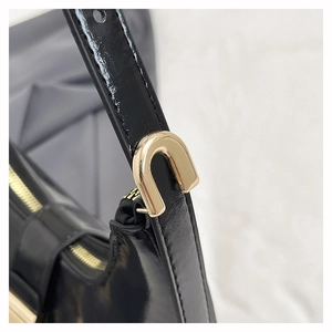Detail of glossy black leather shoulder bag with a polished gold U-shaped metal buckle