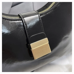 Detail of glossy black leather handbag showing gold metal buckle and textured zipper