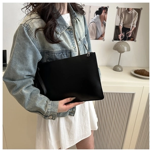 Close-up of a black leather clutch bag with a sleek wristlet strap and metallic zipper