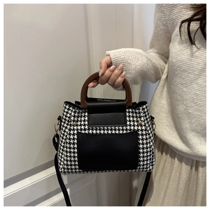 Close-up of houndstooth handbag featuring a round wooden handle and leather details