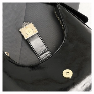 Close-up of gloss black leather bag featuring gold magnetic hardware and premium stitching