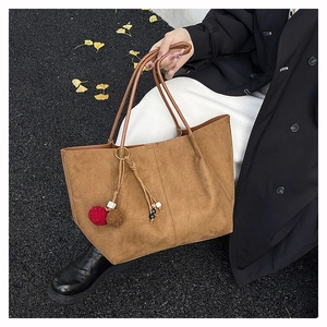 Brown suede tote bag with decorative pom-poms shown in an autumn outdoor lifestyle setting