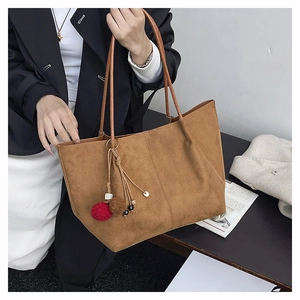 Close-up of brown matte suede tote bag with decorative red pom-pom charm and long handles