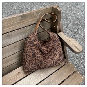 Détail du sac cabas léopard avec anses en cuir marron posé sur un banc en bois