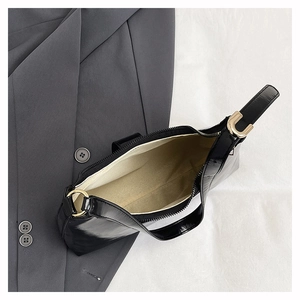 Detail of black glossy shoulder bag showing golden hardware and light beige fabric lining