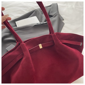 Detail view of burgundy suede tote bag with golden buckle and sleek shoulder strap
