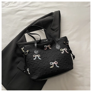 Détail du sac matelassé noir avec broderies de nœuds colorés posé sur un blazer sombre