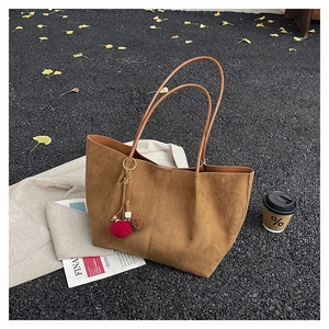 Brown frosted suede tote bag with decorative pom-poms and beads on dark gravel ground