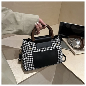 Detail of houndstooth crossbody bag featuring vintage wooden handle and leather pocket