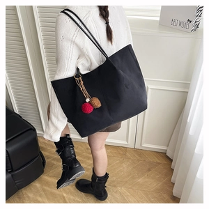 Large black tote bag with plush charms shown on model wearing white knit sweater